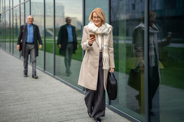 Mature businesswoman using smartphone walking city street