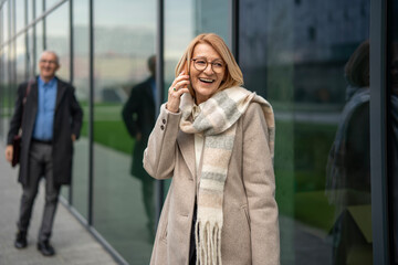 Fototapeta premium Senior businesswoman communicating on smartphone while walking outdoors