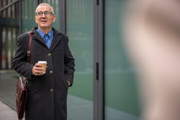 Senior businessman walking with coffee in urban setting