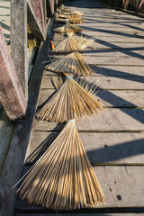 Fototapeta premium Palm Frond Brooms Drying on Sunlit Wooden Pier Walkway