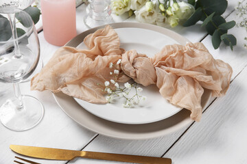Wedding table setting with napkin, flowers, eucalyptus branch and glass on white wooden background