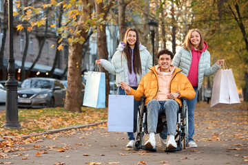 Fototapeta premium Young man in wheelchair and his friends with shopping bags on autumn day