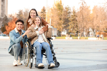 Fototapeta premium Young woman in wheelchair with her friends hugging on city square