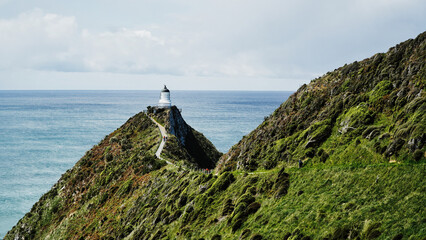 Nugget Point lighthouse with green slopes and blue sea horizonNew Zealand