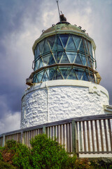 Nugget Point New Zealand lighthouse with glass panels on white brick base under cloudy sky