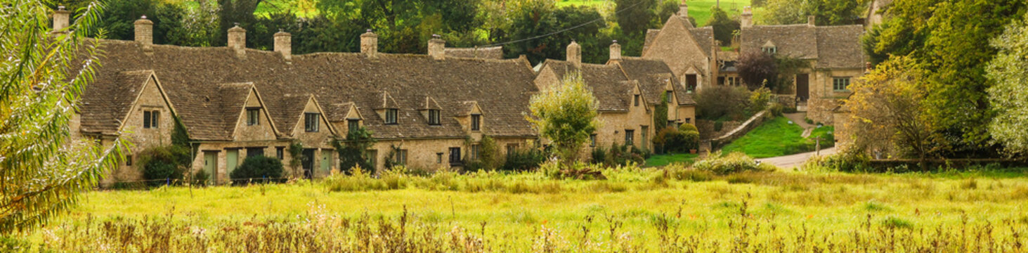 Arlington Row Cotswolds cottages standing behind a vibrant green meadow in the picturesque village of Bibury, England