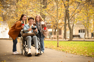 Young man in wheelchair and his friends with coffee taking selfie on street