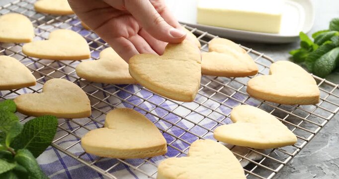Woman taking tasty heart shaped butter cookie from cooling rack at grey textured table, closeup
