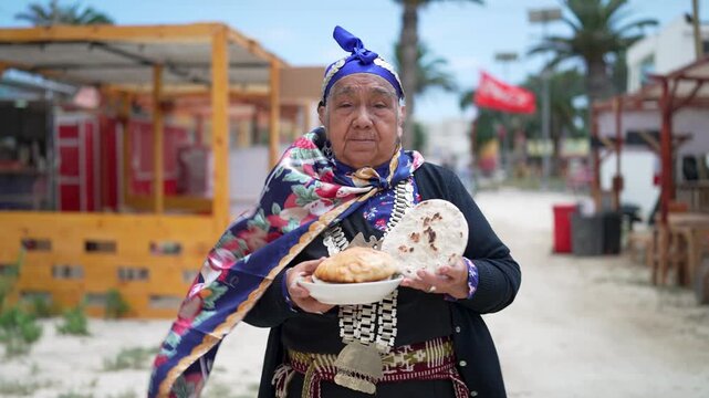 Elderly indigenous woman in traditional clothing holding a plate with homemade bread