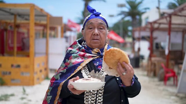 Elderly indigenous woman in traditional clothing offering freshly baked bread at a local food market