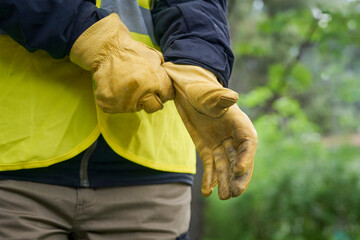 Unrecognizable woman wearing work clothes and a reflective vest adjusts her leather gloves before...