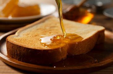 Pouring Fresh Golden Honey onto a Toasted Bread Slice for Breakfast, Delicious Organic Sweetener on Wooden Plate with Copy Space