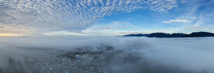 Aerial View Over Foggy Town in British Columbia, Canada With Mountain Range and Clear Sky