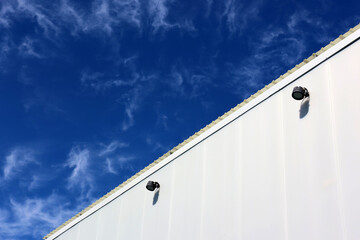Industrial building with white exterior and corrugated roof against a blue sky with wispy clouds background abstract