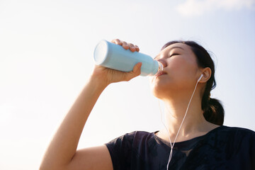 Asian woman drinking water after outdoor workout with earphones
