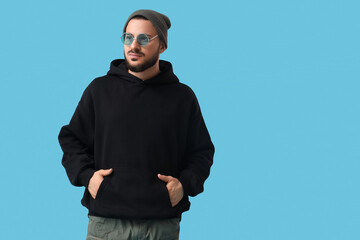 Fototapeta premium Stylish young man in black hoodie on blue background