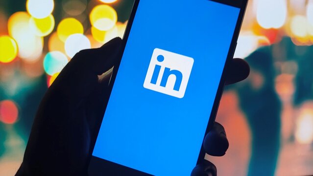 Hand holding smartphone with LinkedIn app on screen at night