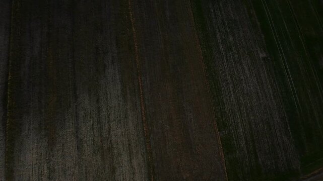 Drone shot of agricultural field from above, showcasing dark soil patterns, aerial farming landscape