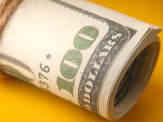 A roll of U.S. one-hundred dollar bills, tied together, against a yellow background