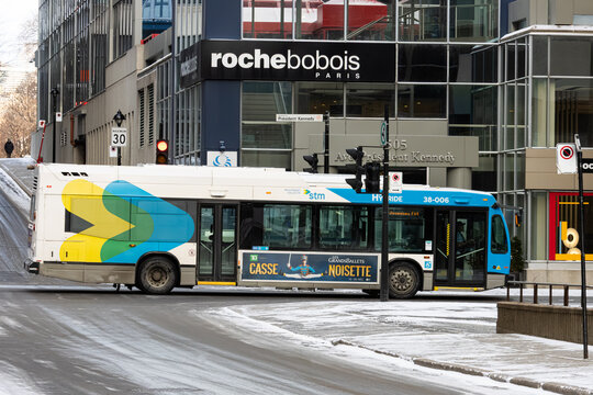 Canada, Montreal, 22 December 2025 : Hybrid city bus passes snowy street beside glass office buildings