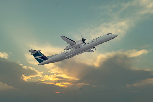 Calgary, Alberta, Canada. January 13, 2026. A WestJet Encore De Havilland Dash 8-Q400 turboprop airplane climbs into a dramatic sunset sky.
