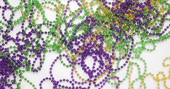 Pile of Mardi Gras beads in yellow or gold green and purple with a large fleur de lis. Throw Mardi Gra bead necklaces covering white background. Celebrating Mardi Gras, aka Fat Tuesday.