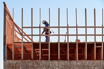 Construction worker assembling wood framing on a commercial building under construction, representing structural installation, exterior development, and active building operations