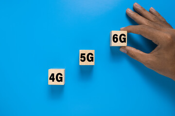 male hand put 4g, 5g, and 6g symbol on wooden blocks. isolated on blue background. concept of wireless telecommunication evolution technology