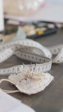 closeup measuring tape and pincushion on wooden table, soft natural light, scattered spools and threads, pins stuck into linen pad, blurred tools in background, warm nostalgic atmosphere for handmade