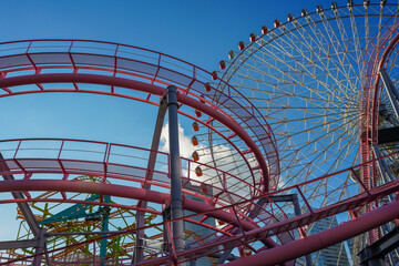 Pink roller coasters and a Ferris wheel at an amusement park against a blue sky on a sunny day. Close-up.