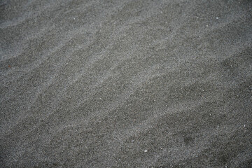 Rippling dark gray sandy surface of the ocean shore. Selective focus. Background. Space for text.