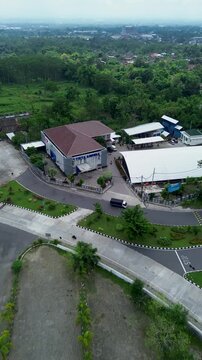An aerial view of the PDAM Ampera building in Boyolali, featuring a spacious roundabout with a central monument, green landscaping, smooth roads, and surrounding urban greenery under a bright sky.