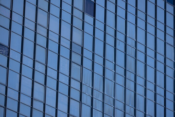 A section of a modern building with many rectangular glass windows reflecting the clear