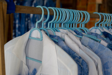 close-up shot of tie-dye t-shirts hanging on light blue plastic hangers. The shirts feature a soft, pastel tie-dye pattern.