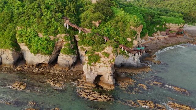 Isolated rock formation separated from a coastal cliff on the Golden Beach near Dalian. Weathered stone stands by the shoreline, highlighting natural erosion and rugged geology.