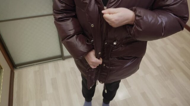 Adult woman indoors zipping and unzipping brown padded jacket, high angle view. Clothing adjustment and daily routine concept.