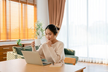 Beautiful young Asian woman working with laptop computer in living room. Work at home