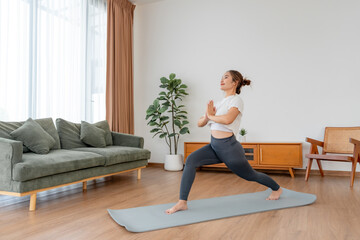 Happy young Asian woman practicing yoga and shoulder stretching  in living room at home