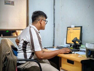 Asian warehouse employee working on a computer with a barcode scanner on his desk. Concepts: logistics management, inventory tracking, supply chain data entry, and industrial office productivity.