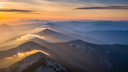 Snowy mountain range at sunrise with fog and clouds aerial view of peaks and valleys in warm light