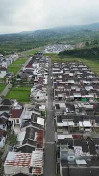 An aerial view of housing development in Wonosobo, showing neat rows of newly built homes, quiet streets, green open land, and a growing residential area blending with the surrounding landscape.