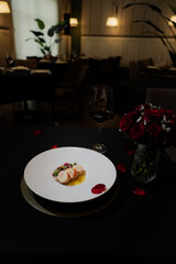 Romantic dinner setting with a beautifully plated dish, a wine glass, and roses. The scene suggests a special occasion with a dark elegant tablecloth, the food presentation shows fine dining