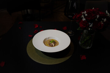 A gourmet meal elegantly served, capturing the essence of fine dining with a romantic touch. A delectable dish within a white bowl is placed atop a green plate, complemented by a bouquet of red roses.