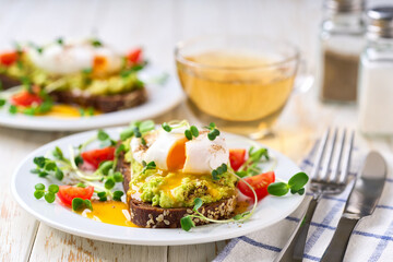 Toast with avocado and egg with cup of tea for healthy breakfast or snack. Sandwich with avocado and poached egg on a white table, selective focus.
