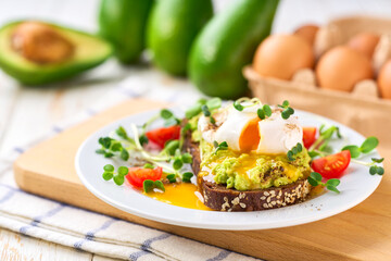 Whole wheat toasted bread with avocado, poached egg, pea sprouts and cheese over white table. Healthy diet breakfast. close up