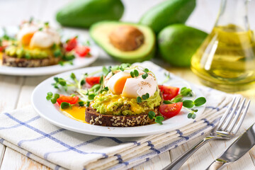 Whole wheat toasted bread with avocado, poached egg, pea sprouts and cheese over white table. Healthy diet breakfast. close up