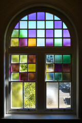 Fototapeta premium Looking from the inside, out to blue skies, through an arched window featuring coloured glass panels - vertical