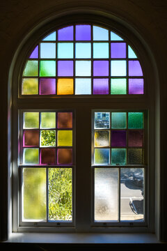 Looking from the inside, out to blue skies, through an arched window featuring coloured glass panels - vertical
