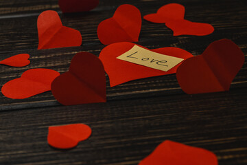 Red paper hearts and a note saying love are scattered on a dark wooden table. The scene is arranged for a celebration or romantic setting.