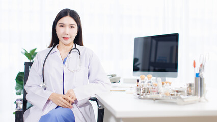 Portrait confident asian female doctor sitting working at desk in professional office medical clinic hospital with computer stethoscope documents system physician expertise in healthcare consultation
